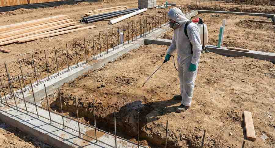 A pest control professional applying soil treatment to a new construction foundation.